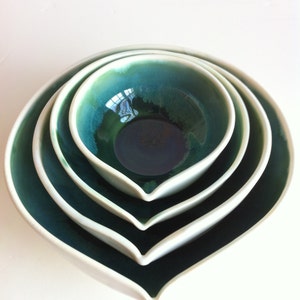 May include: Set of four nesting bowls in a heart shape. The bowls are made of ceramic and have a green and white glaze. The bowls are nested inside each other, with the smallest bowl at the top.