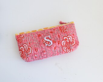 May include: A pink quilted zippered pouch with a floral print and a white embroidered letter "S" on the front.