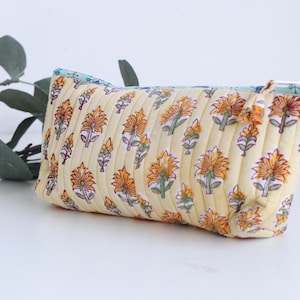 May include: A rectangular, quilted cosmetic bag with a floral pattern in yellow, orange, and green. The bag has a light yellow background and a blue and green interior. The bag is approximately 9 inches long.