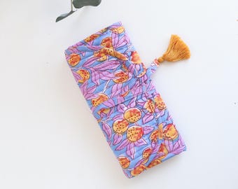 May include: A quilted pouch with a floral pattern in shades of blue, purple, and orange. The pouch has a drawstring closure and a gold tassel. The design features stylized flowers and leaves.