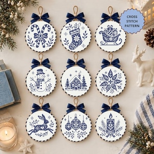 May include: Nine circular cross stitch patterns featuring dark blue holiday designs on white fabric, including candy canes, a stocking, a sleigh, a snowman, a house, a poinsettia, a rabbit, ornaments, and a candle, with text CROSS STITCH PATTERN.