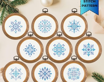 May include: Nine mini cross stitch patterns in wooden hoops, each featuring a unique blue and teal snowflake design. The hoops are arranged in a circular pattern, with a banner that reads "MINI CROSS STITCH PATTERN".