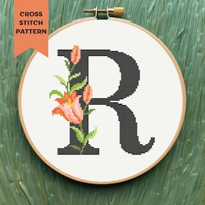 Könnte beinhalten: Kreuzstichmuster des Buchstabens R mit orangefarbenen Blumen und grünen Blättern. Das Muster befindet sich in einem runden Stickrahmen.