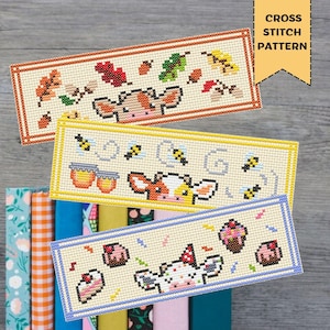 May include: Three cross-stitch bookmarks with cow designs. One features autumn leaves, another bees and honey, and the third cupcakes and party decorations. The text "CROSS STITCH PATTERN" is in a yellow banner.
