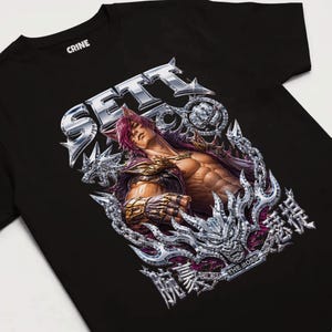 May include: A black t-shirt featuring a graphic print of a muscular character with purple hair and animal ears. The design includes metallic silver chains, a dragon-like emblem, the text SETT, THE BOSS, and Japanese characters in a chrome style.