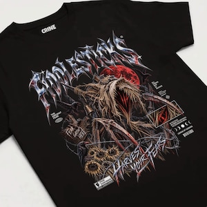 May include: A black t-shirt featuring a graphic print of a scarecrow-like figure with straw-like textures, a red moon, and crows. The text includes "CRINE," "THE ANCIENT FEAR," "FEAR GROWS HERE," "HARVEST YOUR FEARS," and "LEAGUE OF LEGENDS" with moon phases.