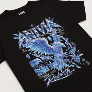 Peut inclure: Un t-shirt noir avec un grand motif métallique représentant un oiseau cristallin bleu. Le design inclut le texte ANIVIA, THE CRYOPHOENIX, REBORN et FRELJORD, ainsi que des phrases plus petites comme FROM FROST REBORN A BRIGHTER TOMORROW.