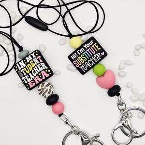 May include: Two black lanyards with key rings. One lanyard has a black square with the text "IN MY STUDENT TEACHER ERA". The other has a black square with the text "Hi! I'm Your SUBSTITUTE TEACHER". Both have colorful beads.