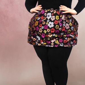 May include: A black skirt featuring a vibrant, all-over sequin floral pattern in shades of red, yellow, pink, and silver. The skirt has a rounded, voluminous silhouette and is worn over solid black leggings with a long-sleeved black top.