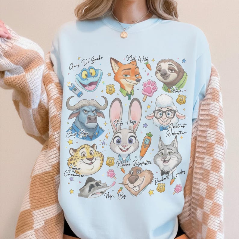 K&ouml;nnte beinhalten: Ein hellblaues Sweatshirt mit Rundhalsausschnitt und einem Grafikdruck verschiedener animierter Tierfiguren, darunter ein Hase, ein Fuchs, ein Faultier und ein Leopard. Das Design enth&auml;lt Textbeschriftungen, kleine Polizeimarken, Karotten und Pfotenabdr&uuml;cke.