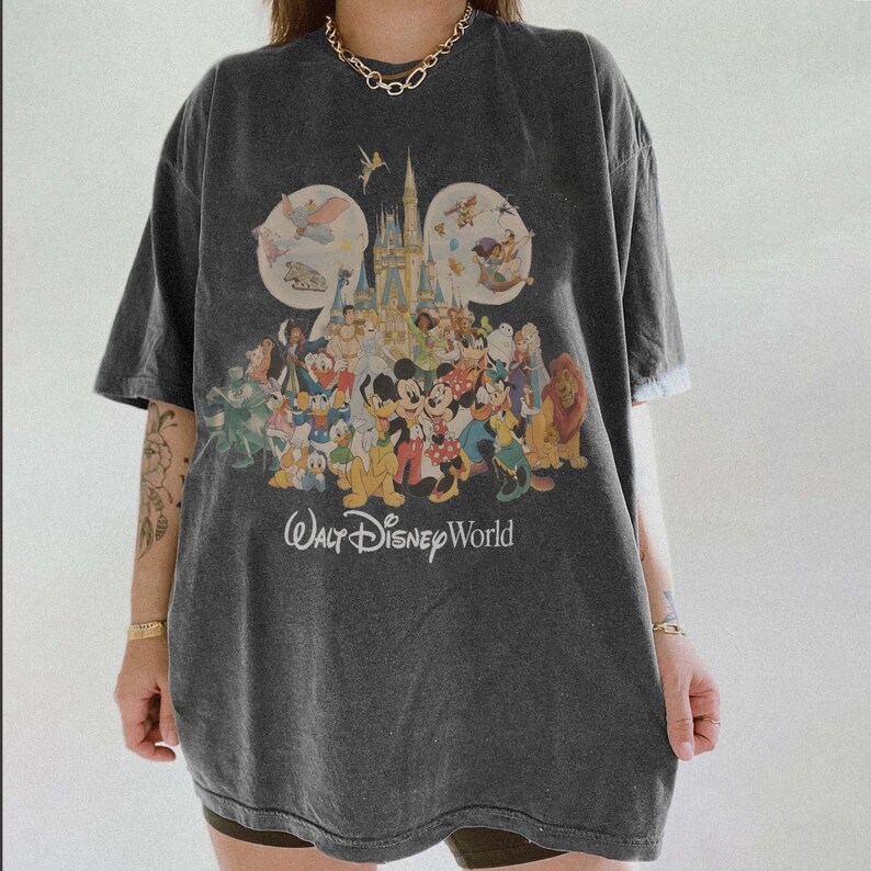 May include: Dark gray t-shirt featuring a colorful graphic of Disney characters and Cinderella's castle. The text "Walt Disney World" is printed below the graphic. The shirt has short sleeves and a relaxed fit.