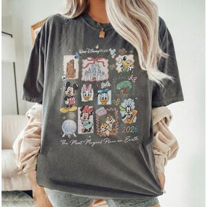 May include: Dark gray t-shirt featuring a collage of Disney characters and landmarks. The design includes Mickey Mouse, Minnie Mouse, Donald Duck, and Chip and Dale, with the text "Walt Disney World" and "The Most Magical Place on Earth".
