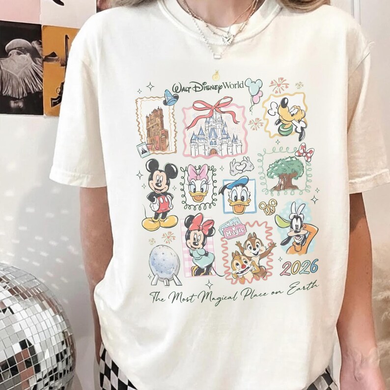 May include: Cream-colored t-shirt featuring a colorful collage of Disney characters and landmarks. The design includes Mickey Mouse, Minnie Mouse, Donald Duck, and Goofy, with the text "Walt Disney World" and "2026". The shirt also has the phrase "The Most Magical Place on Earth".