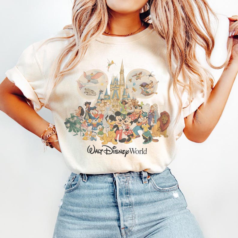 May include: Cream-colored t-shirt featuring a colorful graphic of Disney characters, including Mickey and Minnie Mouse, in front of a castle. The words "Walt Disney World" are printed below the graphic.