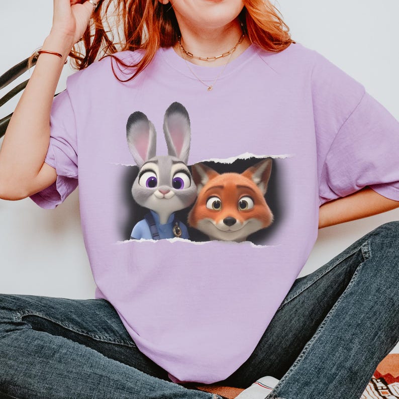 K&ouml;nnte beinhalten: Ein helllila T-Shirt mit einer Grafik von Judy Hopps und Nick Wilde aus Zoomania. Die Zeichentrickfiguren sind in einem zerrissenen Papiereffekt dargestellt. Das Shirt ist ein kurz&auml;rmeliges Rundhals-Shirt.