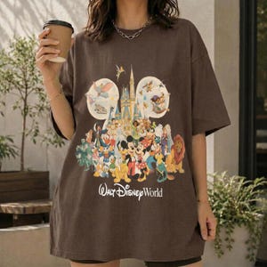 May include: Brown t-shirt featuring a colorful graphic of Disney characters, including Mickey Mouse, Donald Duck, and Simba, in front of a castle. The words "Walt Disney World" are printed below the graphic. The shirt has short sleeves.