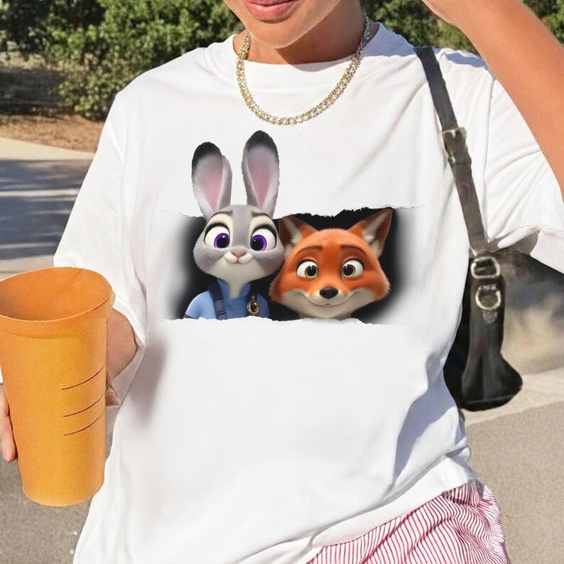 K&ouml;nnte beinhalten: Wei&szlig;es T-Shirt mit einer Grafik von Judy Hopps und Nick Wilde aus Zoomania. Die Zeichentrickfiguren sind in einem zerrissenen Papiereffekt dargestellt. Das Shirt besteht aus einem weichen Material.