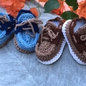Puede incluir: Tres pares de zapatos de beb&eacute; de ganchillo en azul, marr&oacute;n y blanco. Los zapatos tienen cordones y un estilo de zapato de barco.