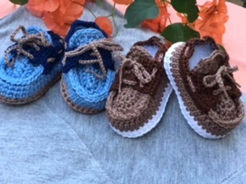 Puede incluir: Tres pares de zapatos de beb&eacute; de ganchillo en azul, marr&oacute;n y blanco. Los zapatos tienen cordones y un estilo de zapato de barco.