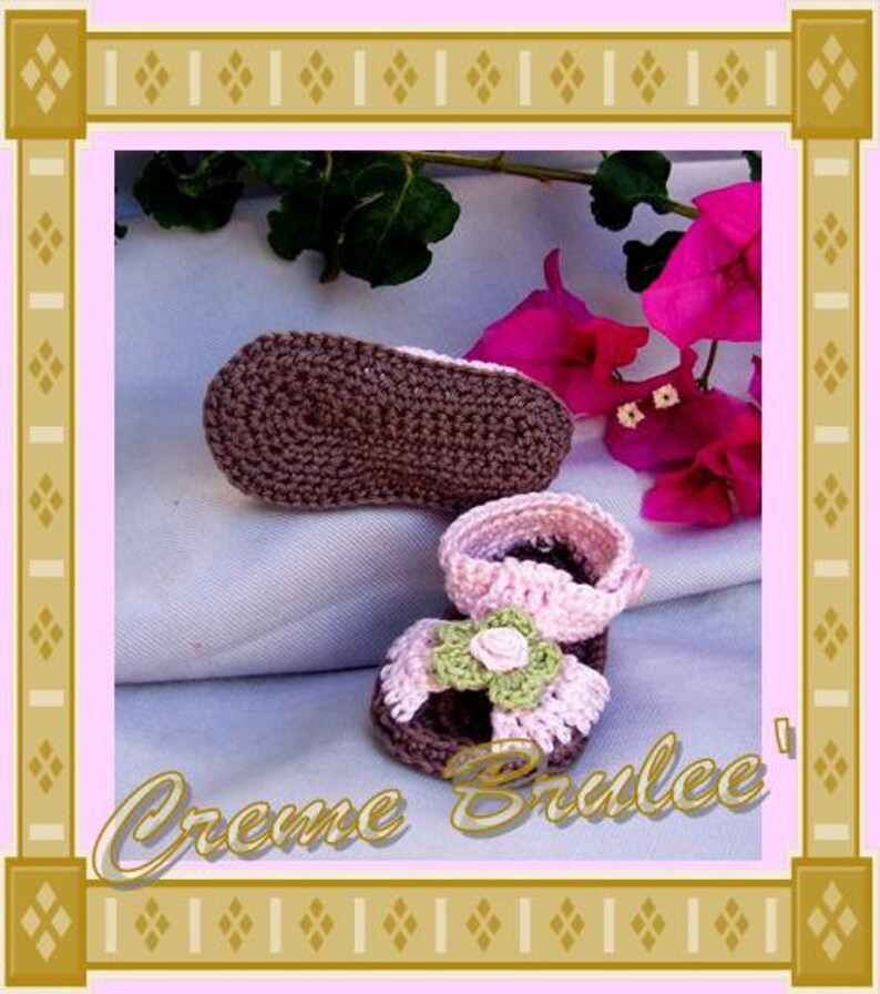 May include: A pair of crocheted baby shoes. One shoe is brown and the other is pink with a green flower embellishment. The shoes are on a white fabric background.