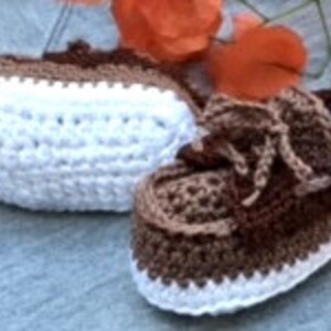 Puede incluir: Un par de botitas de beb&eacute; de ganchillo de color marr&oacute;n y blanco con cordones. Las botitas tienen una suela blanca y una parte superior marr&oacute;n con un patr&oacute;n de rayas marrones y blancas.