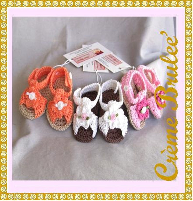 May include: Five pairs of crocheted baby sandals in orange, white, and pink with flower embellishments. The sandals are handmade and have a delicate, feminine design.