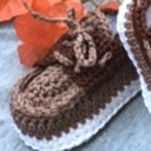 Puede incluir: Botitas de beb&eacute; de crochet marr&oacute;n y blanco con cordones. Las botitas tienen un dise&ntilde;o texturizado y un ribete blanco.