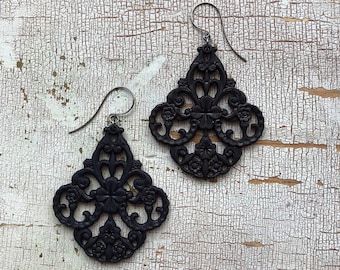 May include: A pair of black filigree earrings with a delicate floral design. The earrings are made of metal and have a hook closure.