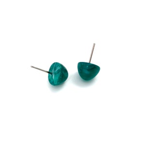 Op de afbeelding: Een paar tealkleurige oorstekers. Elke oorbel heeft een afgeronde, halve koepelvorm met een zilveren pin. De oorbellen hebben een gemarmerd uiterlijk, met wervelingen van lichtere en donkerdere teal. De achtergrond is wit.