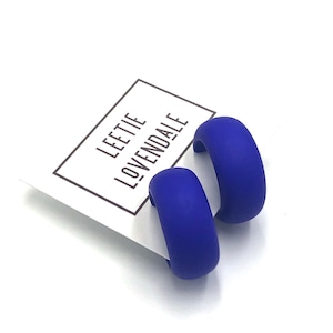 May include: A pair of blue matte hoop earrings. The earrings are made of a thick, rounded material and have a smooth finish.