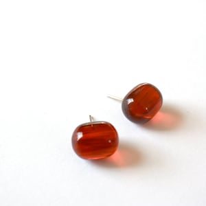 May include: A pair of brown glass earrings with silver posts. The earrings are oval shaped and have a slightly textured surface.