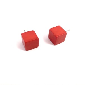 May include: A pair of red cube-shaped stud earrings. The earrings are made of a smooth, glossy material.