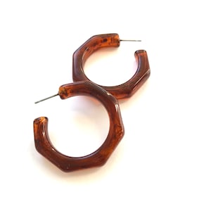 May include: A pair of brown resin hoop earrings with a hexagonal shape. The earrings are simple and elegant.