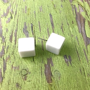 May include: A pair of white cube stud earrings. The earrings are made of a smooth, white material and have a simple, modern design.