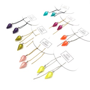 May include: Assortment of colourful teardrop-shaped earrings with long chains. The earrings are displayed on white cards with the text "Leetie Lovendale" printed on them.
