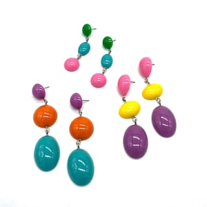 May include: Three pairs of drop earrings featuring smooth, glossy, multi-colored oval beads arranged in vertical clusters. The earrings showcase vibrant shades of green, blue, pink, orange, yellow, and purple, all connected by silver-toned metal posts.