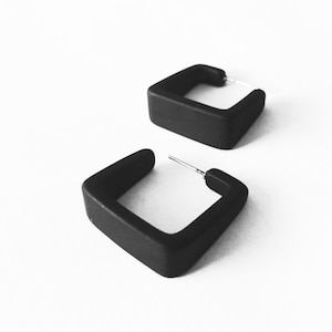 May include: A pair of black square hoop earrings. The earrings are made of a smooth, matte material.