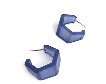 May include: A pair of blue hexagonal hoop earrings. The earrings are made of a smooth, matte material and have a simple, modern design.