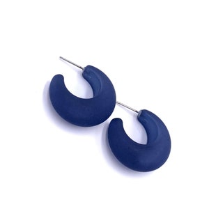 May include: A pair of blue hoop earrings. The earrings are made of a smooth, matte material and have a slightly rounded shape.