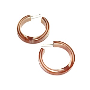 May include: A pair of brown and white hoop earrings. The earrings are made of a thick, round, plastic material with a swirl pattern.