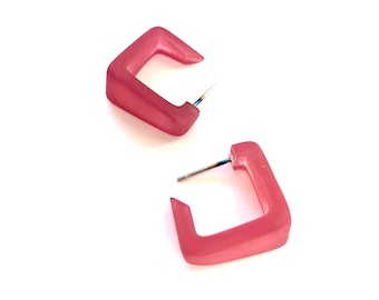 May include: A pair of pink square hoop earrings. The earrings are made of a translucent material and have a slightly frosted finish.
