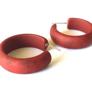 May include: A pair of red hoop earrings. The earrings are made of a thick, matte material and have a slightly textured surface.