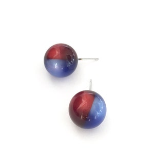 May include: A pair of stud earrings with a red and blue iridescent finish. The earrings are round and have a silver post.