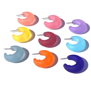 May include: Eight pairs of colorful hoop earrings. The earrings are made of a translucent plastic material and come in a variety of colors, including blue, purple, pink, yellow, orange, and red.