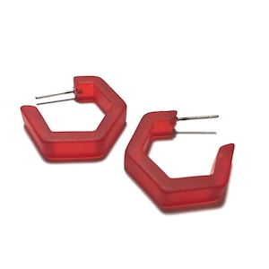 May include: A pair of red hexagonal hoop earrings. The earrings are made of a translucent plastic material.