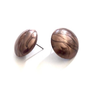 May include: A pair of round, brown and gold earrings with a marbled pattern. The earrings are made of metal and have a post back.