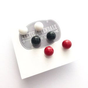 May include: A set of six small round earrings in white, black, and red.