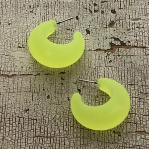 May include: A pair of neon yellow hoop earrings. The earrings are made of a smooth, matte material and have a simple, modern design.