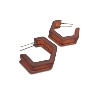 May include: A pair of brown hexagonal hoop earrings. The earrings are made of a smooth, matte material.