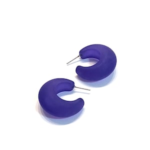 May include: A pair of purple hoop earrings. The earrings are made of a smooth, frosted plastic.